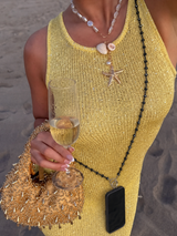 Person in yellow dress holding a glass of champagne on a beach