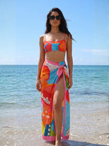 Woman in a colorful bikini and sarong standing on a beach.
