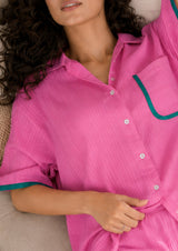 Woman wearing a pink shirt with green trim, lying on a beige surface.