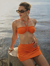 Woman in an orange bikini sitting by a body of water.