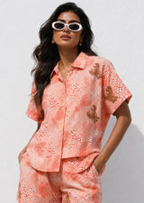 Woman wearing a coral floral outfit with sunglasses against a white background