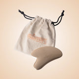 Gua Sha tool with a branded drawstring bag on a beige background
