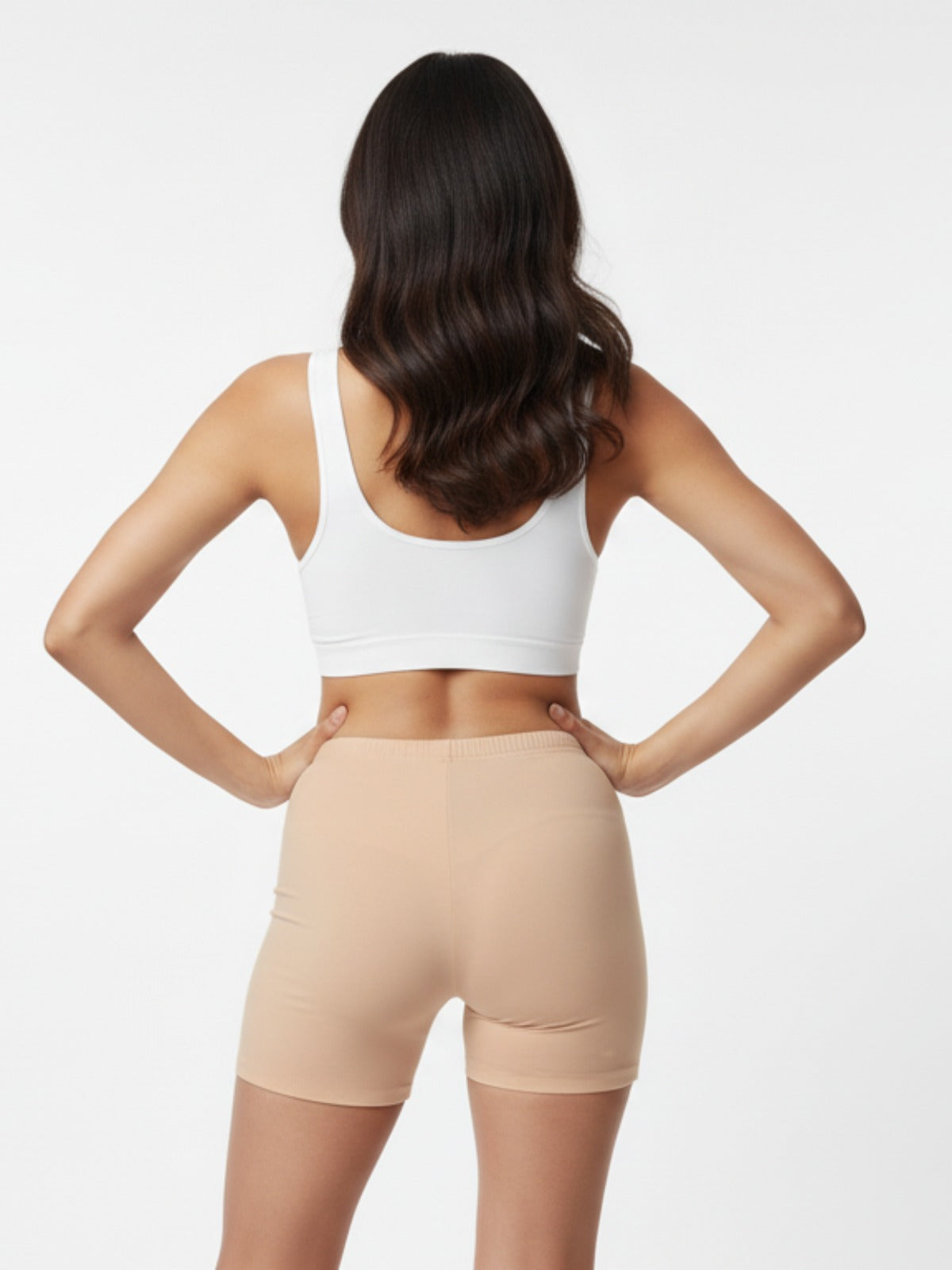 Woman wearing beige shapewear shorts and a white crop top on a light gray background
