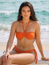 Woman in an orange bikini sitting on a beach with ocean waves in the background