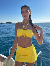 Woman in a yellow bikini and skirt on a boat with blue water and sky in the background
