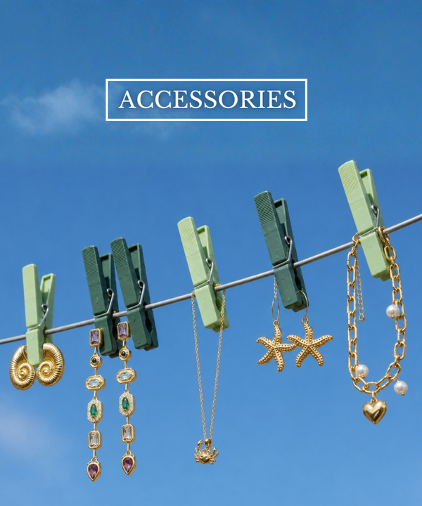 A collection of gold-toned jewelry clips and necklaces hanging from a clothesline with green wooden clothespins against a bright blue sky. The text 'ACCESSORIES' is displayed at the top.