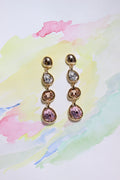 Pair of Auric Petals Earrings with pink and clear gemstones on a colorful watercolor background