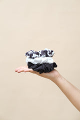 Hand holding three black and white patterned scrunchies