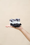 Hand holding three black and white patterned scrunchies