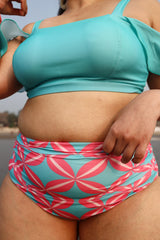 Plus size woman wearing a turquoise bikini top and pink and blue patterned shorts