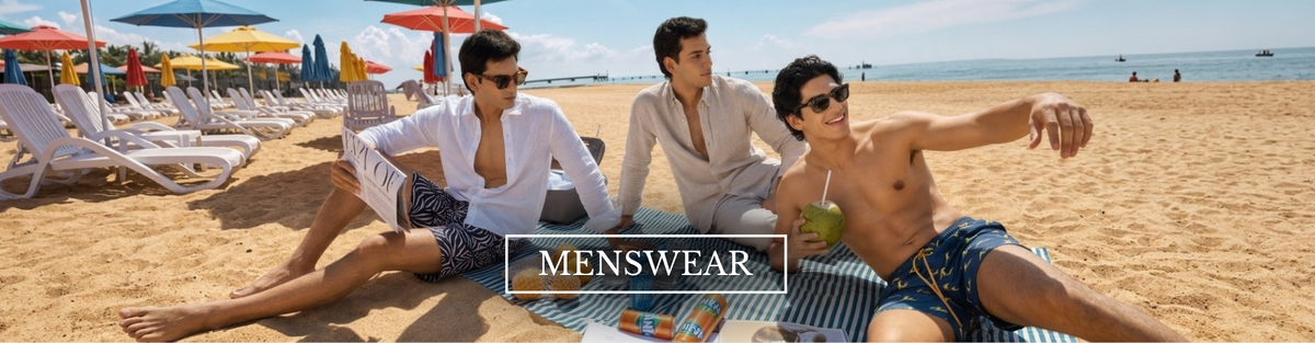 Three men relaxing on a sandy beach under colorful umbrellas, wearing casual summer clothing and swim trunks. A banner at the bottom reads 'MENSWEAR'.