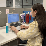 Person working on a laptop at a desk with a red mug and blue bottle.