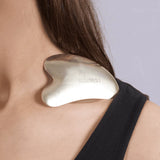 Person wearing a gold gua sha tool on their shoulder with a neutral background