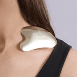 Person wearing a gold gua sha tool on their shoulder with a neutral background