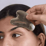 Person using a Gua Sha tool on their face against a neutral background