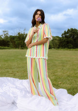 Woman in a colorful striped outfit holding a flower in a field