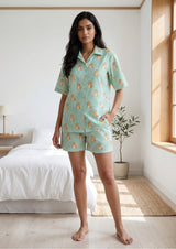 Woman wearing a green patterned pajama set in a bedroom.