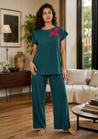 Woman wearing teal pajama set with floral embroidery in a living room.