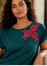 Woman wearing a teal top with pink floral embroidery
