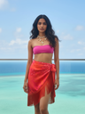 Woman in a pink top and red sarong standing by a pool with ocean view