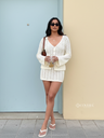 Woman in a white outfit standing against a light blue wall.
