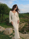 Woman in a white lace dress standing in a natural landscape with greenery and rocks.