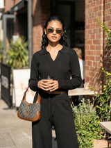 Woman in black ribbed crop top and pants outfit holding a coffee cup and a brown handbag outdoors.