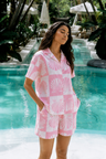 Woman in a pink and white patterned outfit standing by a pool with greenery in the background