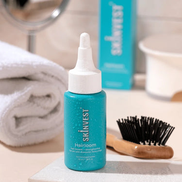 Blue bottle of Skinvest Hairloom on a bathroom counter with a brush and towel in the background.