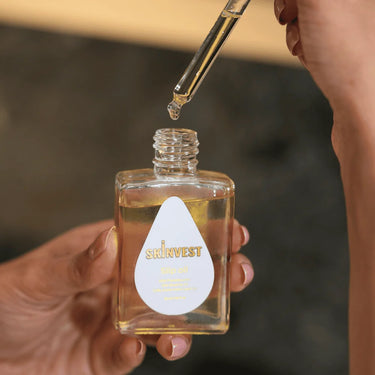 Hand holding a bottle of skincare product with a dropper, brand 'SINVEST' visible.