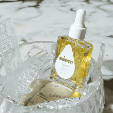 Skincare dropper bottle labeled 'skinvest' on a decorative stand with ice-like texture.