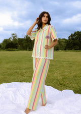 Woman in a colorful striped outfit standing in a grassy field with trees in the background.