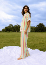 Woman in a striped outfit standing on a blanket in an open field with trees in the background.