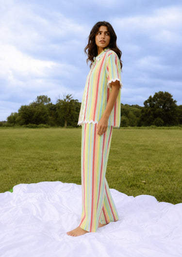 Woman in a striped outfit standing on a blanket in an open field with trees in the background.