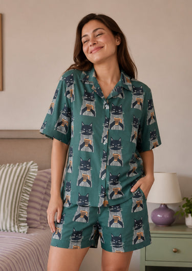 Woman wearing a teal pajama set with cat pattern in a bedroom setting