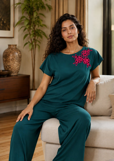 Woman in teal outfit with pink floral embroidery sitting on a couch in a living room.